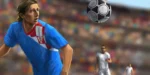 Mladi nogometaš duge kose u plavom dresu vodi loptu pred punim stadionom